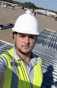 Nick Nowak, Operations Manager at LB Roofing and Construction, on a job wearing a hard hat and safety vest